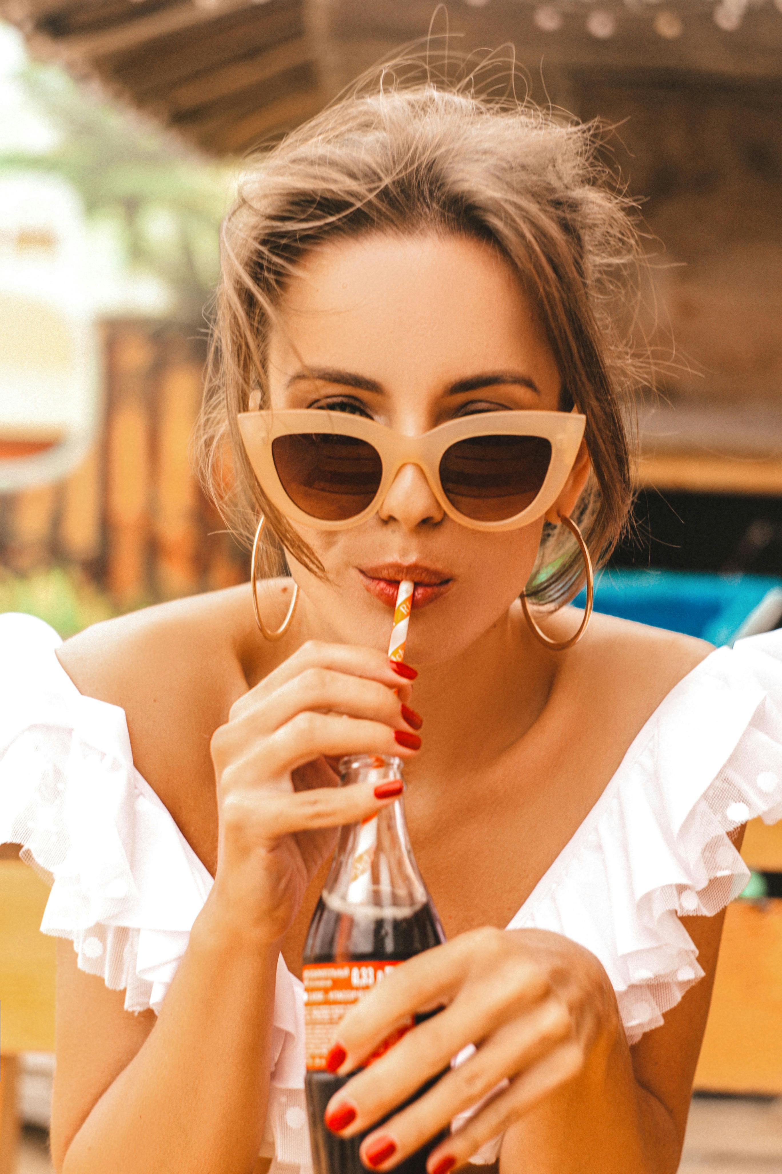 Chic woman wearing sunglasses enjoys a refreshing beverage outdoors. Perfect for summer vibes.