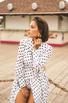 Stylish woman in a dotted dress poses gracefully outdoors, exuding modern fashion elegance.