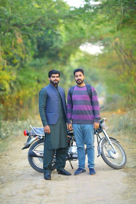 Two men, one in traditional Pakistani attire and one in casual wear, stand by a motorcycle in Kasur, Pakistan. - travel handbag selection Pakistan