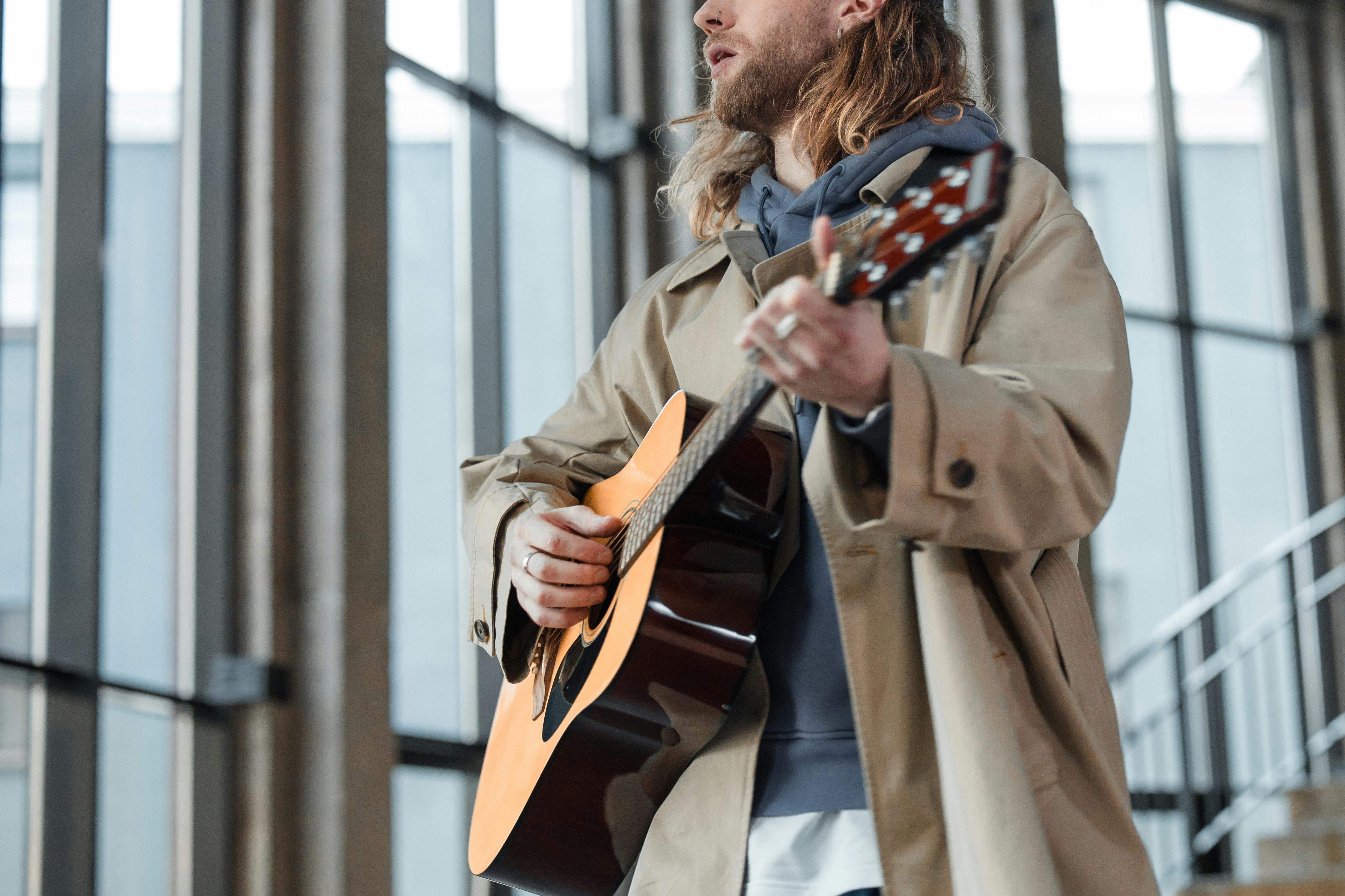 Man in Brown Coat Strumming Brown Acoustic Guitar