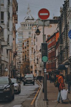 Urban street with people walking, cars passing, and vintage architecture setting a bustling scene.