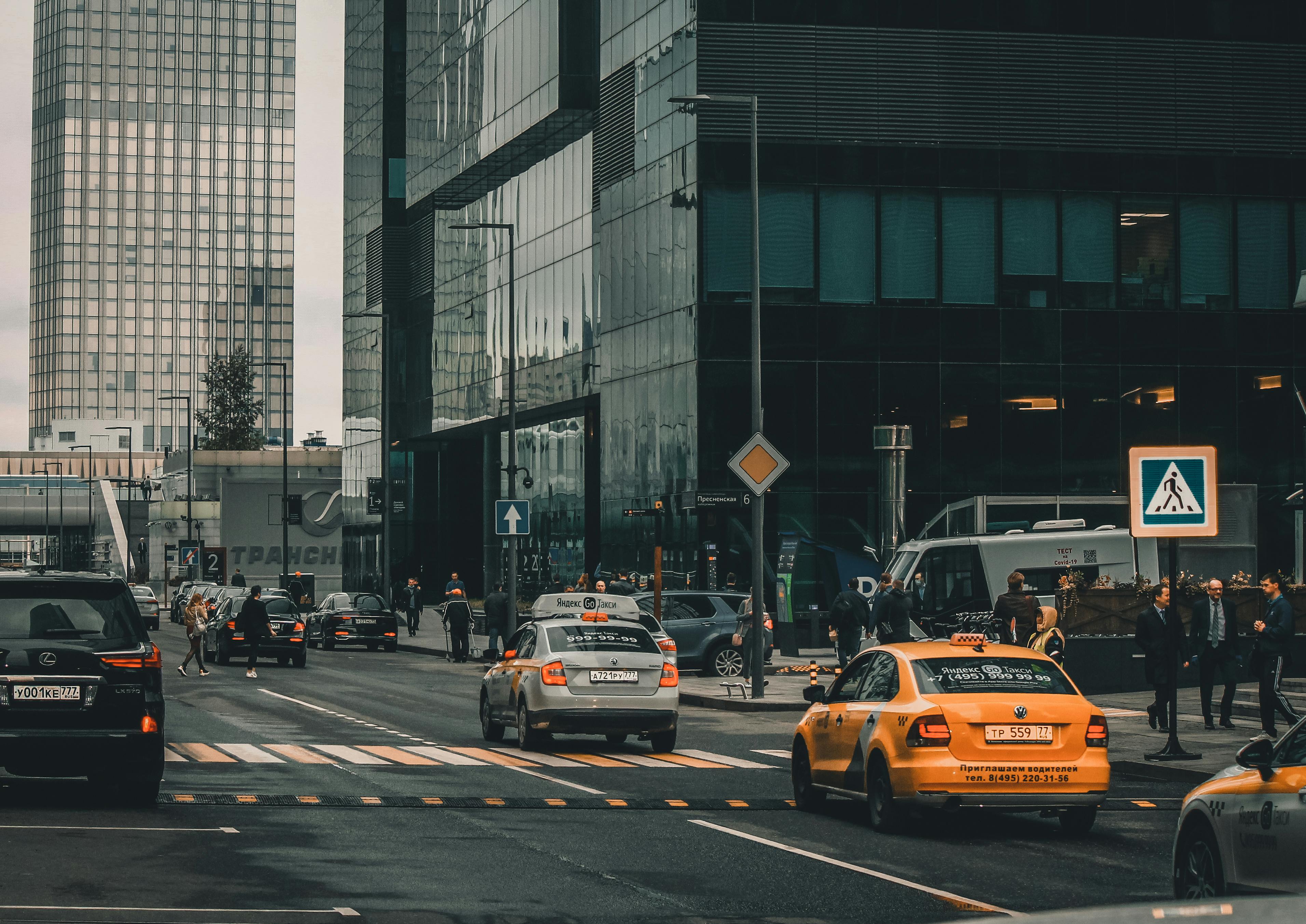 Dynamic city street scene with taxis, tall buildings, and pedestrians, showcasing urban life.