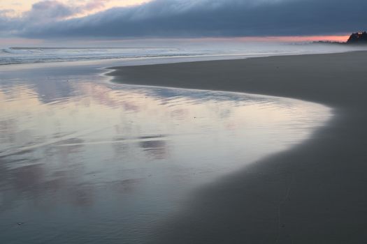 Peaceful beachscape with gentle ocean waves and reflective sandy shores at dawn.