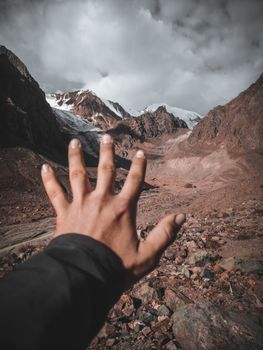 A hand reaching towards scenic mountains, capturing nature's beauty and adventure outdoors.