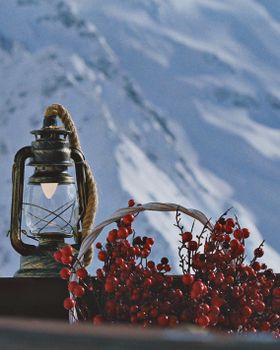 A vintage lantern and red berries create a cozy winter scene against a snowy backdrop.