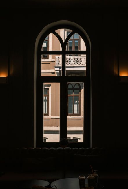 A stylish interior view through an arched window revealing a classic urban building facade.
