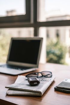 A close-up of a desk setup with a laptop, smartphone, and newspaper, perfect for business themes.