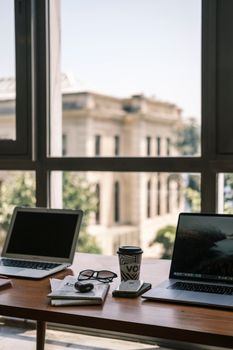 Bright office setting with laptops, coffee, and a city view from a window, ideal for productivity themes.