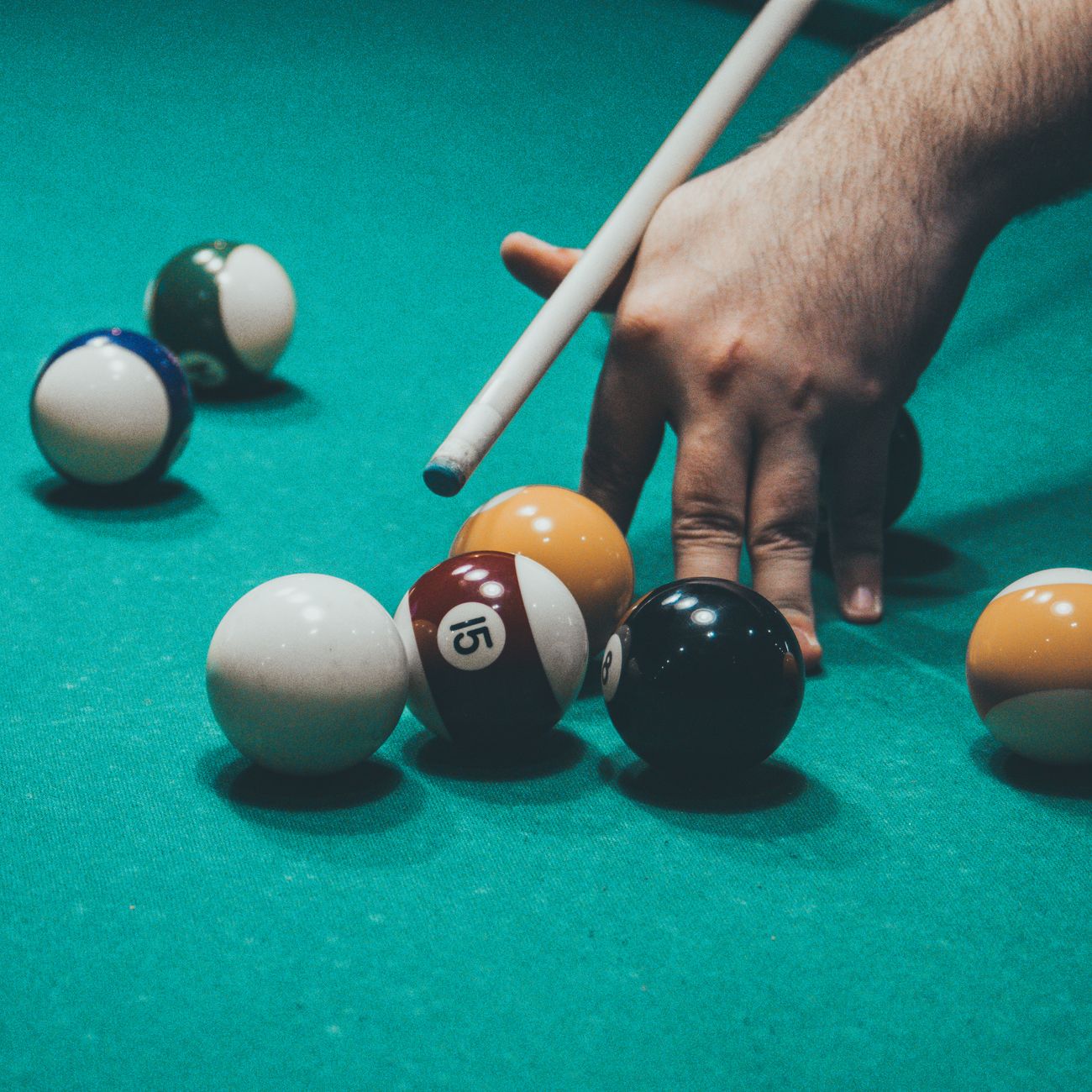 Hand aiming with cue stick in an intense billiards game.