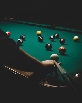 Intense billiards game showing a player's hand aiming the cue stick at the balls on the table.