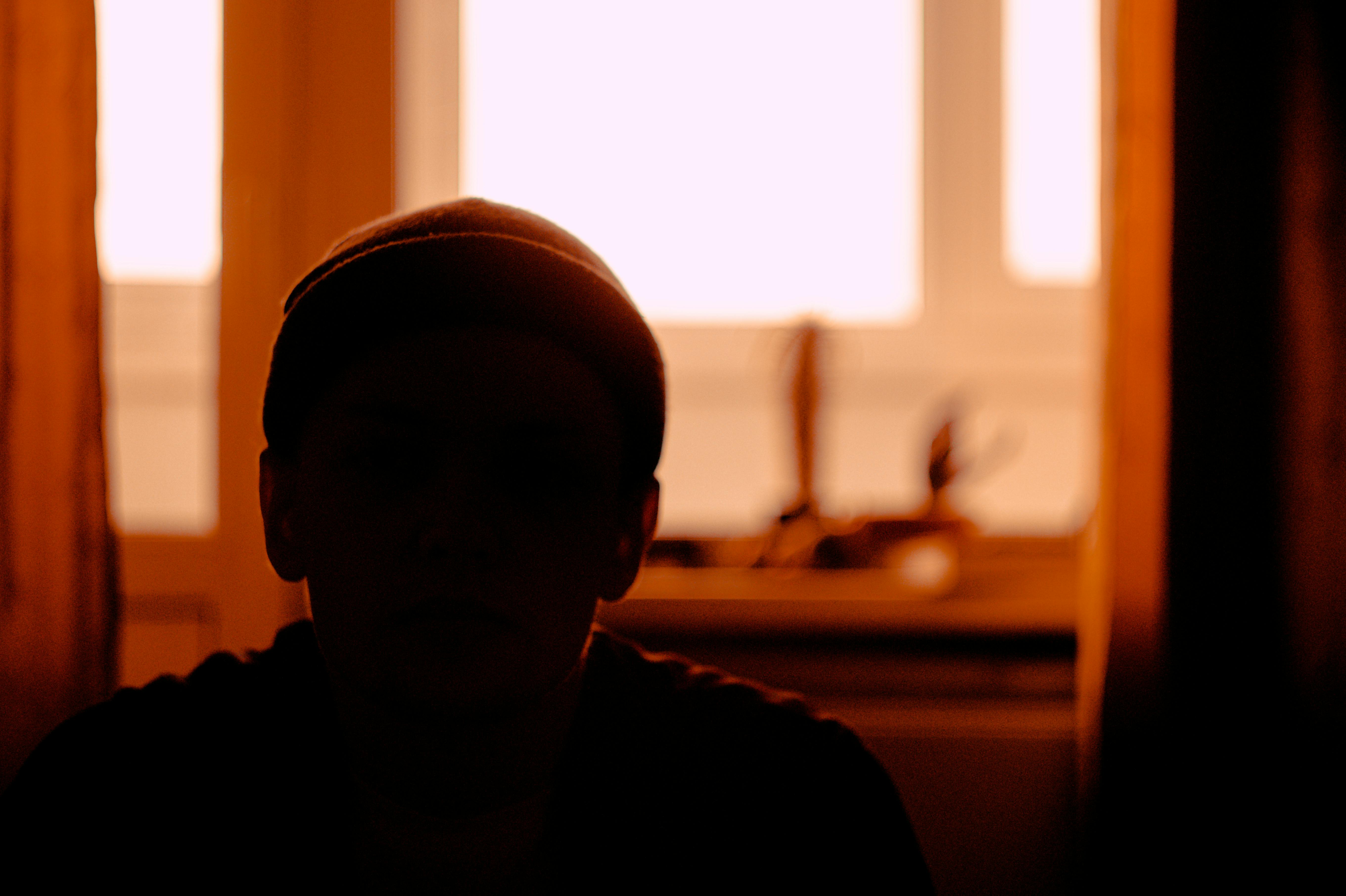 Dramatic silhouette of a person sitting indoors with a warm orange sunset backdrop.