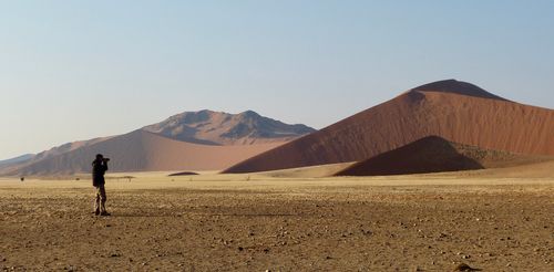 Free A lone photographer captures the stunning beauty of vast desert dunes under a clear sky. Stock Photo