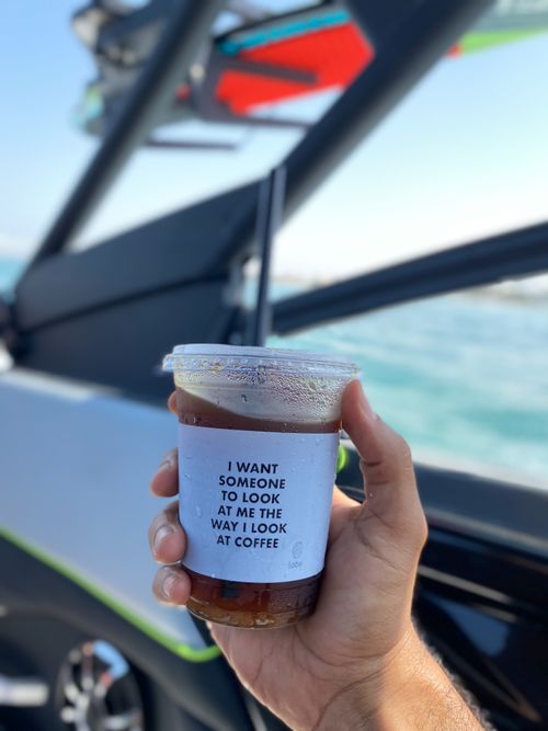 Free Close-up of a hand holding iced coffee with a humorous sleeve on a boat. Stock Photo