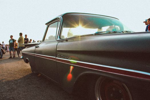 Classic Chevrolet El Camino parked under bright sunlight, surrounded by people at an outdoor event.