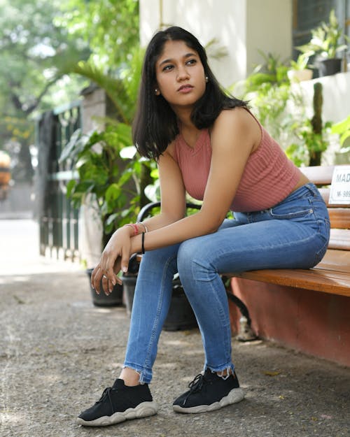 Photo of a Young Woman in Denim Jeans Sitting on a Bench