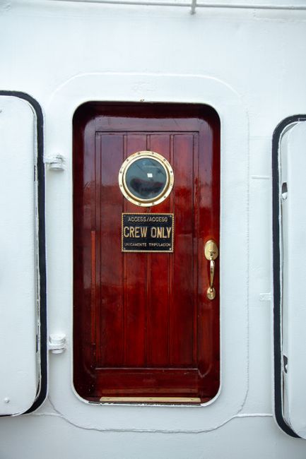 Photo of a 'Crew Only' sign on a red wooden ship door with a porthole.