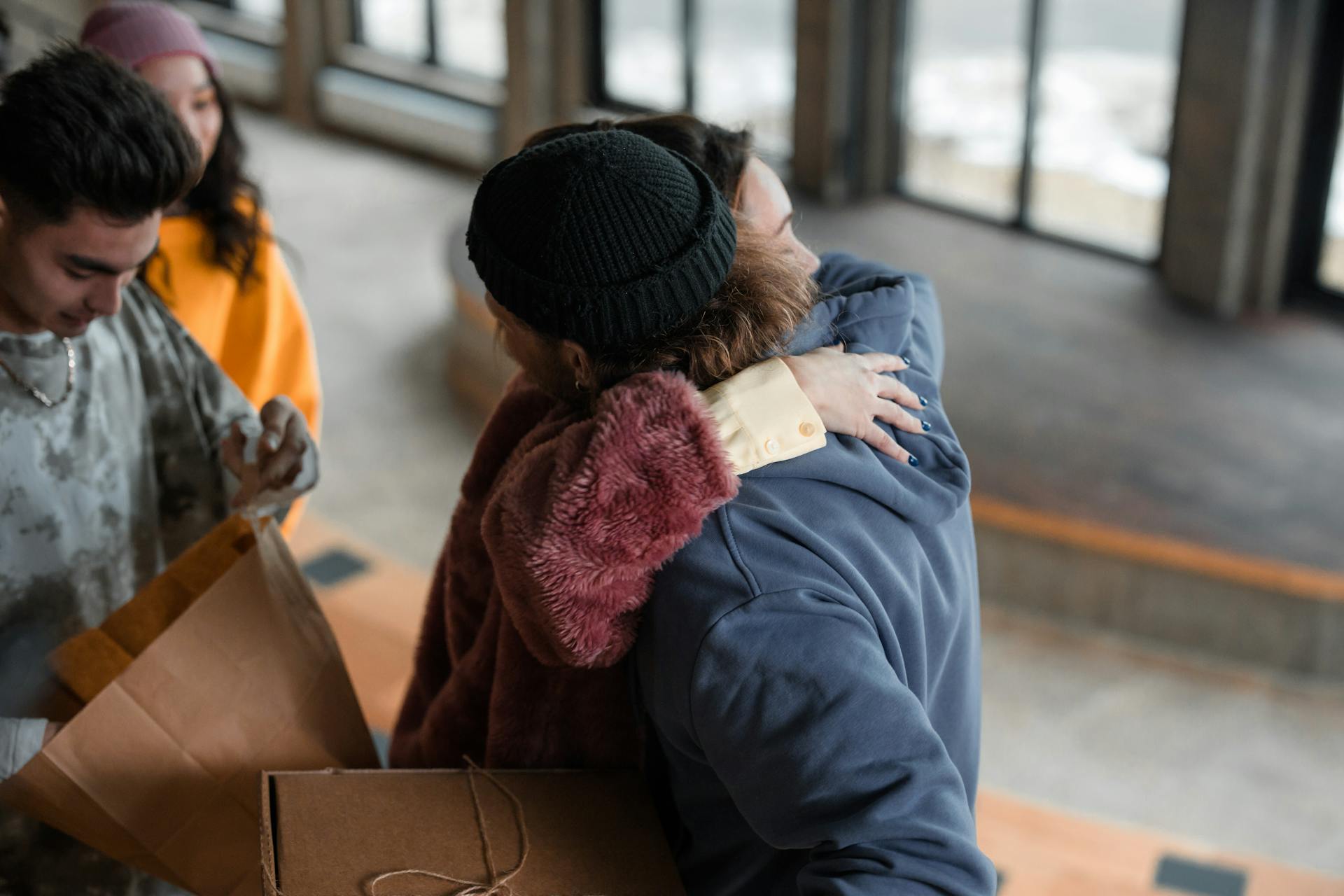 A group of young adults sharing a warm embrace with gift exchange indoors.