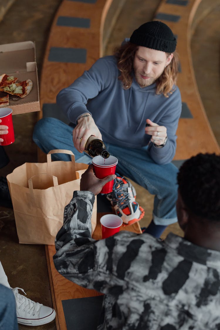 Photo Of A Man With A Black Beanie Pouring Wine Into A Red Cup