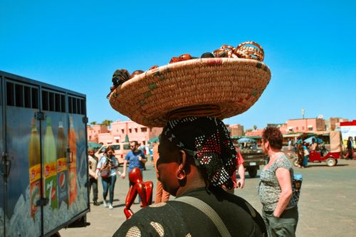 Free An outdoor market scene with a woman balancing a woven basket on her head, surrounded by people. Stock Photo