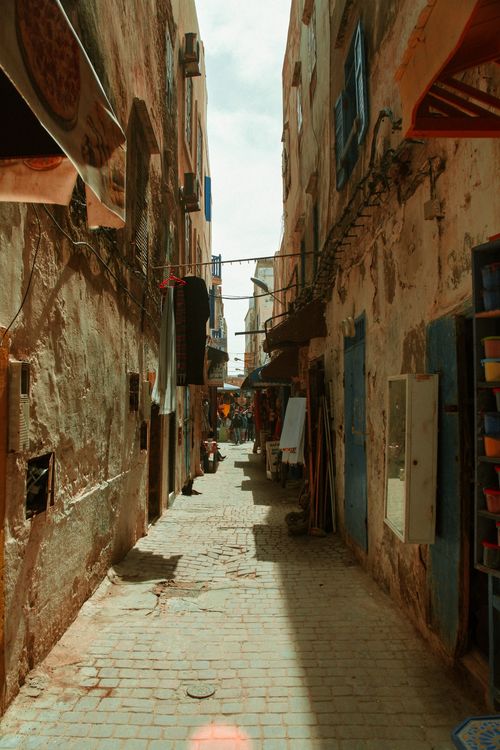 Free Narrow cobblestone alleyway with weathered buildings in a sunlit old town setting. Stock Photo