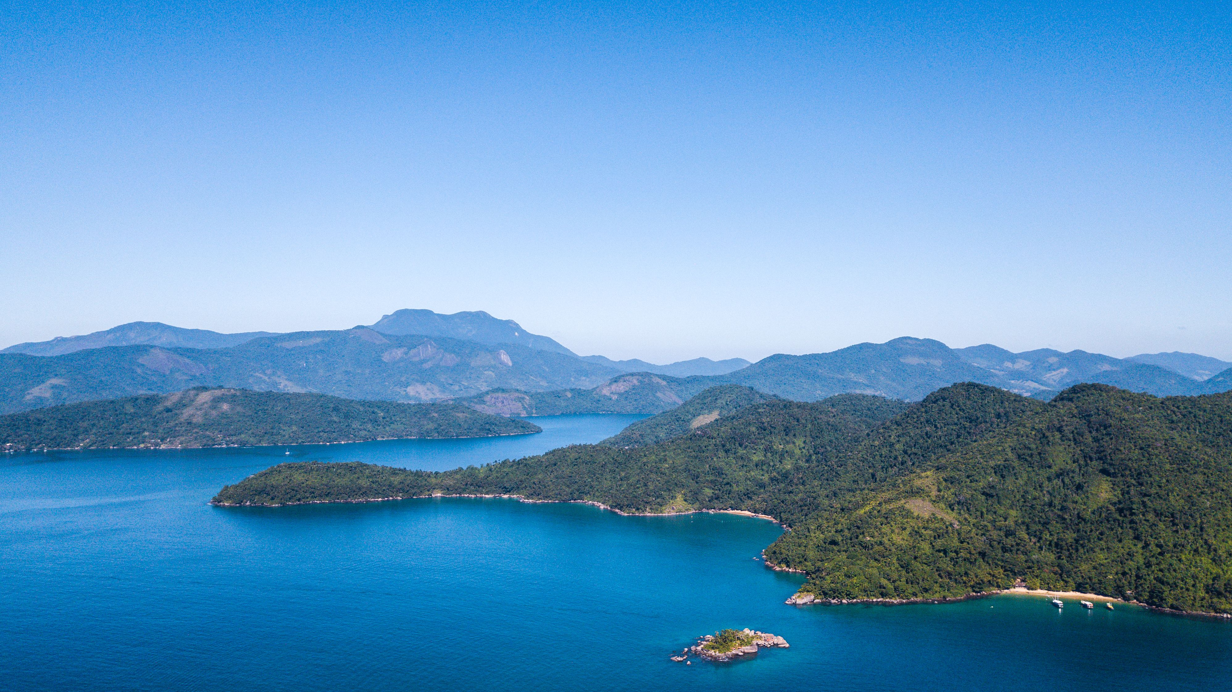 Traditional escuna boat sailing in the clear waters of Paraty Bay, Brazil, with lush islands in the background.