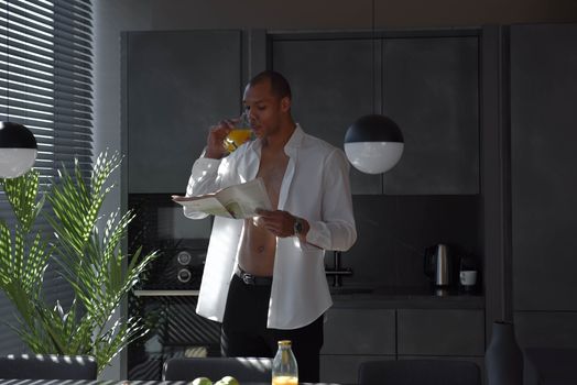 Man in a stylish kitchen reading a newspaper while enjoying a glass of orange juice.