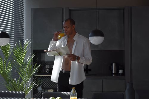 Free Man in a stylish kitchen reading a newspaper while enjoying a glass of orange juice. Stock Photo