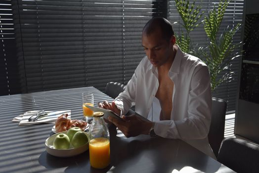 A man in white shirt using tablet at breakfast table enjoying a healthy meal.