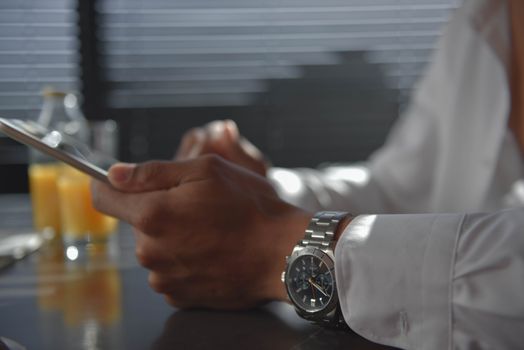 A man wearing a wristwatch holding a tablet in a softly lit room. Morning ambiance.