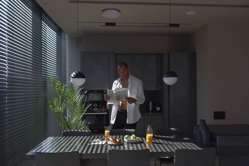 Free A man reads a newspaper in a stylish kitchen with breakfast items and natural lighting. Stock Photo