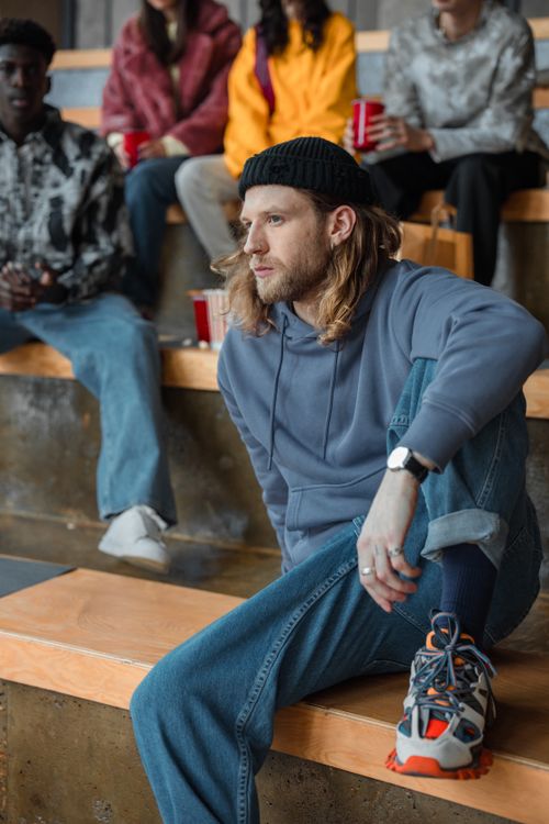 Free Man in casual attire sitting on steps with friends in an urban setting. Diverse group scene. Stock Photo