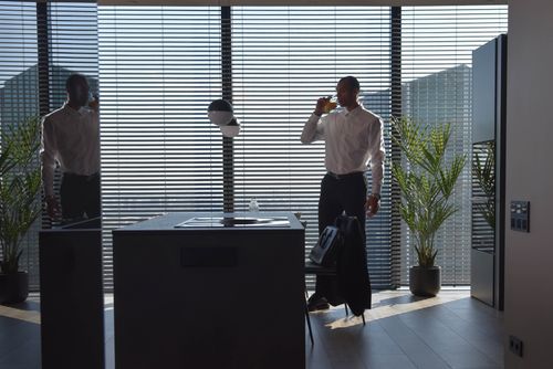 Free Professional scene of a businessman drinking in a contemporary office space with tall window blinds. Stock Photo