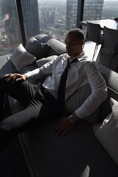 A businessman in a tie sitting on a sofa in a modern office with a city view.