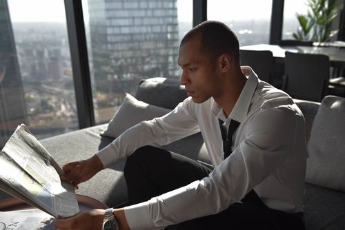 Free Young professional reading a newspaper in an urban office with cityscape view. Stock Photo