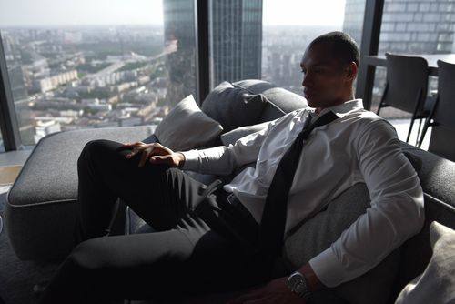 Free A businessman in formal attire relaxes on a sofa enjoying a high-rise city view. Stock Photo