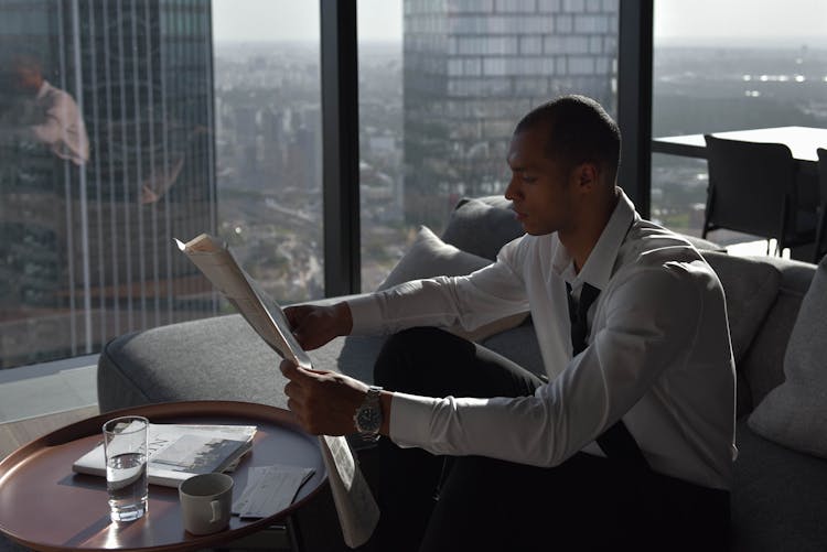 A Man In White Long Sleeves Sitting On The Couch While Reading Newspaper