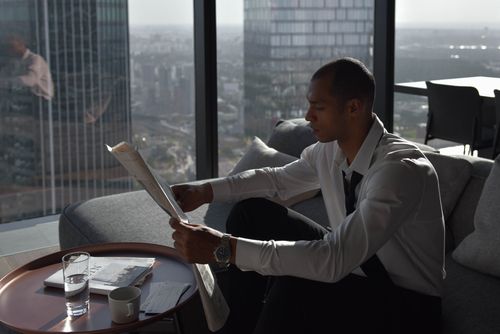 Free A businessman reads a newspaper by the window with a city view from a high-rise apartment. Stock Photo