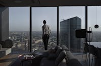 Man in a modern apartment with a panoramic view of an urban skyline and skyscraper