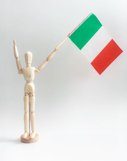 Free A wooden mannequin figurine holds an Italian flag on a white background, symbolizing patriotism. Stock Photo