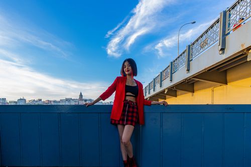 Free Stylish woman in red blazer poses by bridge under clear blue sky. Stock Photo