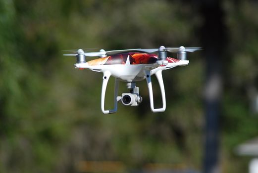 A white drone hovers with a blurred natural background, highlighting its technology and flying capabilities.