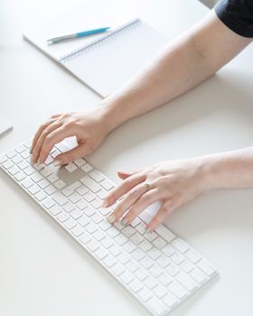 Close-up of hands typing on a sleek white keyboard in a bright minimalist office setting.