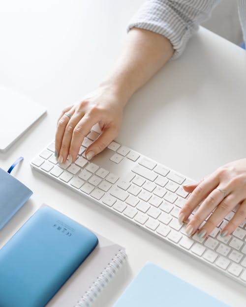 Free Person in White Long Sleeve Shirt Using White Computer Keyboard Stock Photo
