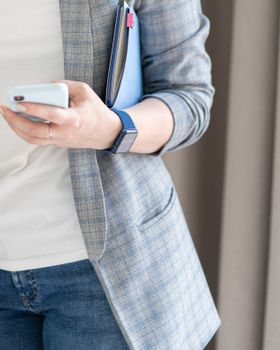 Close-up of a professional woman using a smartphone and holding a folder in an office environment.