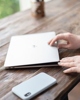 Person interacting with laptop and smartphone on a wooden table, focus on gadgets.