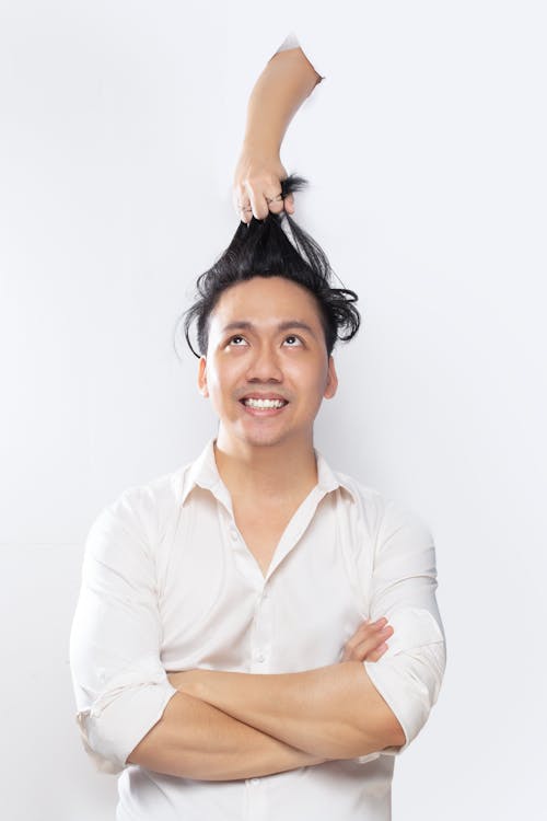 A Man in White Long Sleeves Looking Up on a Hand Pulling His Hair