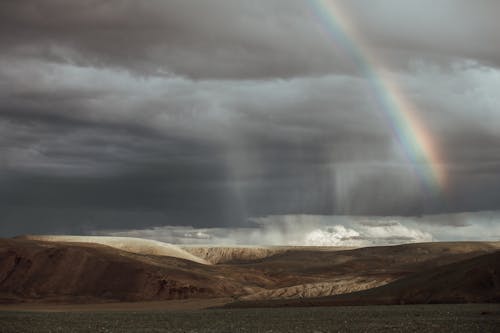 Free Rainbow in the Gray Sky Above Mountains and Sea Stock Photo