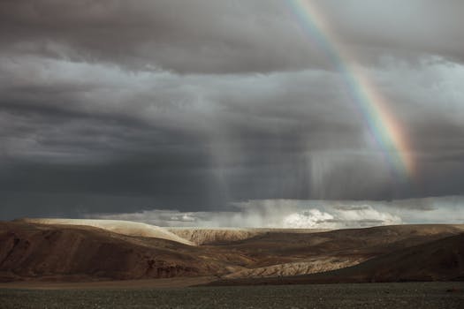 Stunning desert landscape with dark clouds and a rainbow arcing across the sky.