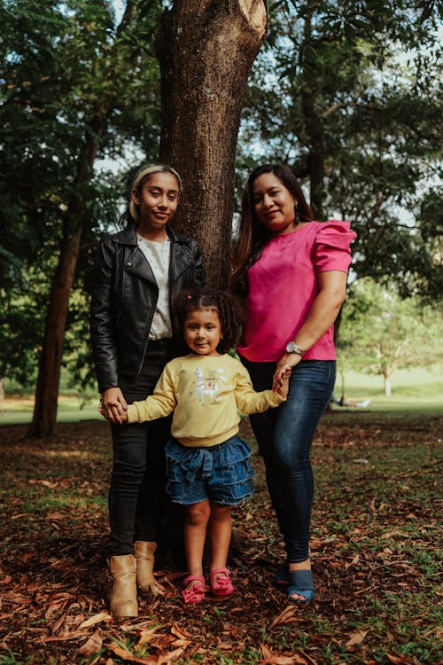 Woman, Teenage Girl and Little Girl Standing Beside Tree Holding Hands