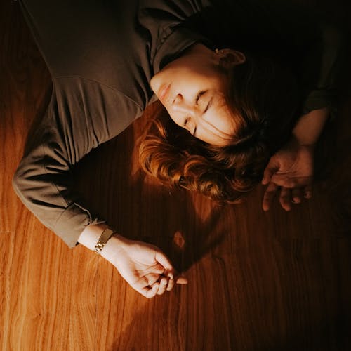 Free Girl Lying on the Wooden Floor Beside Source of Light Stock Photo